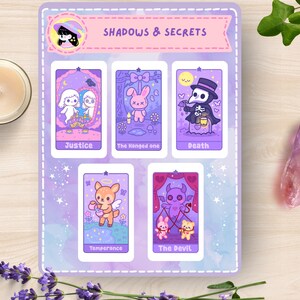 May include: A sticker sheet with the text "Shadows & Secrets" and illustrations of tarot cards. The cards feature whimsical characters and symbols in shades of purple, pink, and white. A lit candle, a crystal, and lavender sprigs are also present.