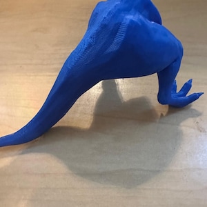 May include: A vibrant blue, 3D-printed sculpture of a creature's leg and body. The sculpture has a textured surface and is resting on a light brown surface. The creature's leg has three toes.