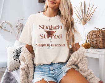 May include: A white t-shirt with the text "Shaken Stirred & Slightly Buzzed" and a graphic of a martini glass with a cinnamon stick.