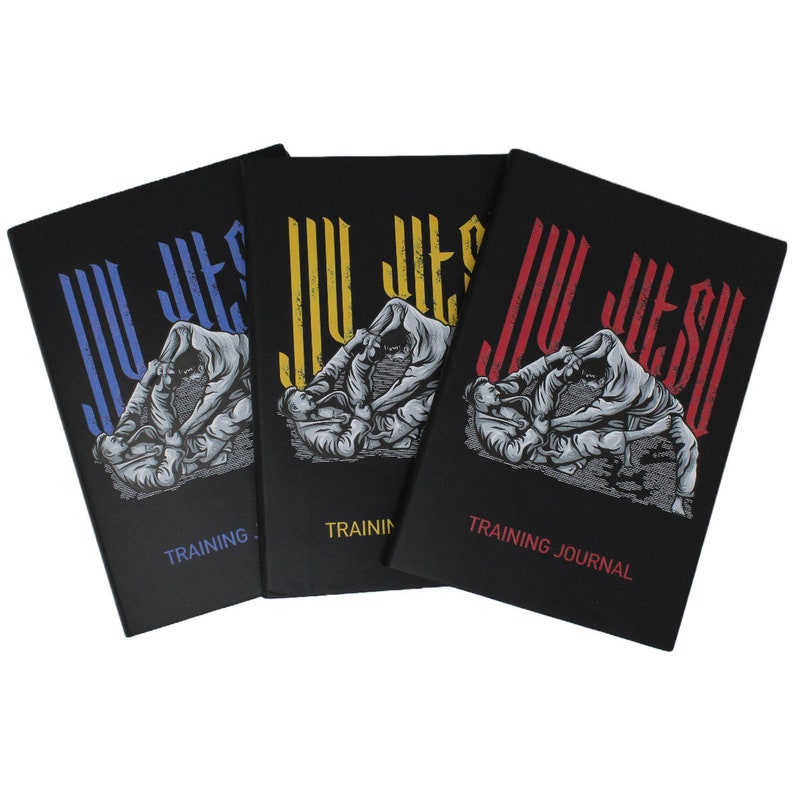 Puede incluir: Tres diarios de entrenamiento negros con el texto "Jiu Jitsu" en una fuente estilizada. Cada diario presenta un color diferente para el texto: azul, amarillo y rojo. Los diarios tienen el texto "Training Journal" impreso en la parte inferior.