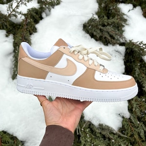May include: A pair of white and beige sneakers with a white swoosh logo and the word "AIR" on the side. The sneakers are tied with white laces.