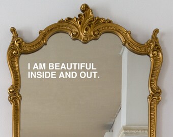May include: A gold-colored ornate mirror with a white inscription that reads "I AM BEAUTIFUL INSIDE AND OUT."