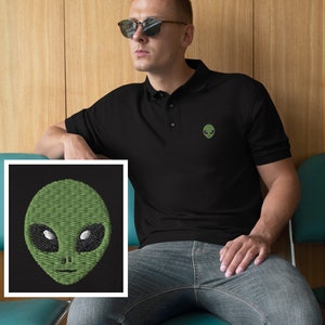 Pu&ograve; includere: Una polo nera con un viso di alieno verde ricamato sul petto sinistro. L'alieno ha occhi grandi e una bocca piccola.