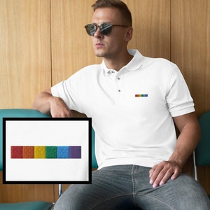 May include: A white polo shirt with a rainbow-colored stripe embroidered on the left chest. The shirt is worn by a person with short brown hair and sunglasses.