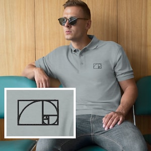 May include: A gray polo shirt with a black embroidered image of the golden ratio spiral on the left chest. The shirt has a button-up collar and short sleeves.