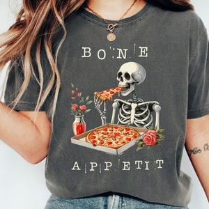 Peut inclure: Un t-shirt gris avec un squelette mangeant une pizza et le texte "BONE APPETIT".
