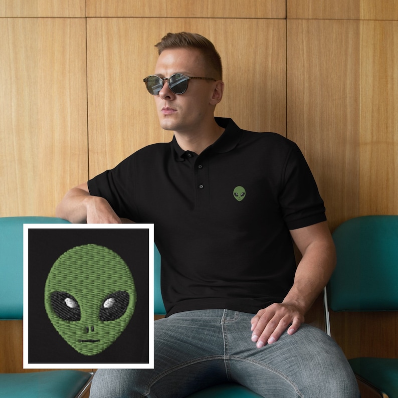 Pu&ograve; includere: Una polo nera con un viso di alieno verde ricamato sul petto sinistro. L'alieno ha occhi grandi e una bocca piccola.
