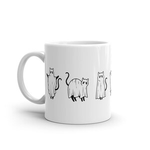 May include: White ceramic coffee mug with a black line drawing of four cats dressed as ghosts. The cats are in a line, facing forward, with their tails behind them.