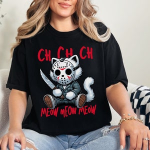 May include: Black t-shirt with a white cat wearing a hockey mask and holding a knife. The text "CH CH CH MEOW MEOW MEOW" is printed on the shirt.
