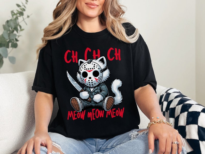May include: Black t-shirt with a white cat wearing a hockey mask and holding a knife. The text "CH CH CH MEOW MEOW MEOW" is printed on the shirt.