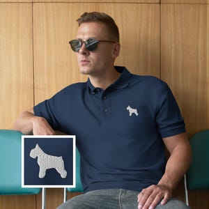 May include: A navy blue polo shirt featuring a white embroidered dog silhouette on the chest. The shirt has a classic collar and button-up placket. The image also shows a close-up of the dog silhouette.