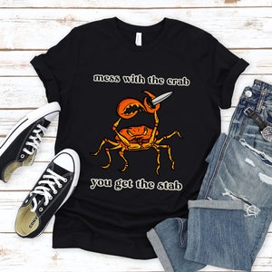 K&ouml;nnte beinhalten: Schwarzes T-Shirt mit einem Grafikdruck eines Krabben, der ein Messer h&auml;lt. Der Text "mess with the crab you get the stab" ist auf dem T-Shirt aufgedruckt.