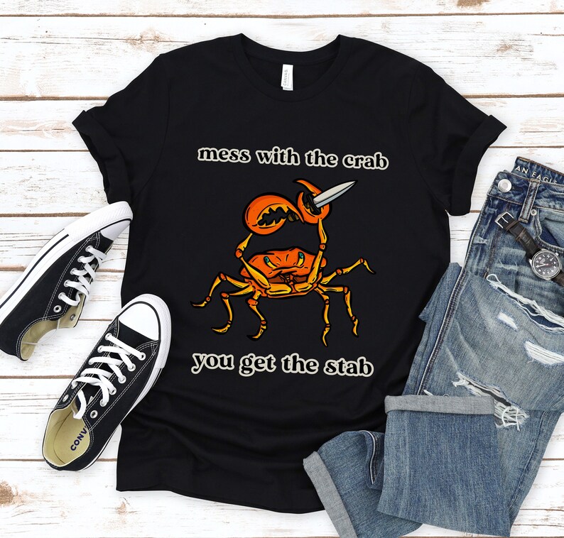 K&ouml;nnte beinhalten: Schwarzes T-Shirt mit einem Grafikdruck eines Krabben, der ein Messer h&auml;lt. Der Text "mess with the crab you get the stab" ist auf dem T-Shirt aufgedruckt.