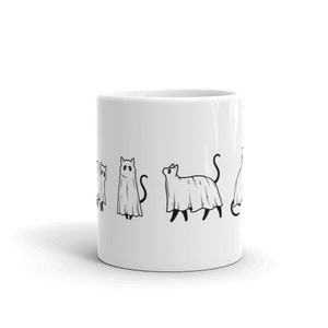 May include: White ceramic coffee mug with a black and white illustration of cats dressed as ghosts. The cats are in various poses, some are standing, some are sitting, and some are walking. The mug is a great gift for cat lovers and Halloween enthusiasts.