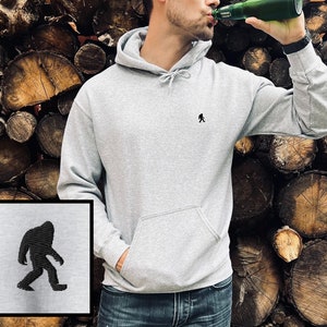Peut inclure: Un sweat &agrave; capuche gris avec une petite silhouette noire de Bigfoot sur le devant. Le sweat-shirt a une poche kangourou et une capuche &agrave; cordon.