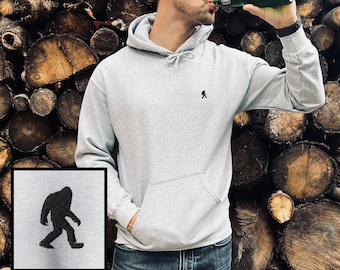 May include: A gray hooded sweatshirt with a small black silhouette of a Bigfoot on the front. The sweatshirt has a kangaroo pocket and a drawstring hood.