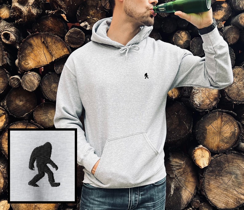 Peut inclure: Un sweat &agrave; capuche gris avec une petite silhouette noire de Bigfoot sur le devant. Le sweat-shirt a une poche kangourou et une capuche &agrave; cordon.