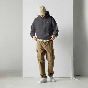 Peut inclure: Un sweat-shirt &agrave; capuche gris fonc&eacute; avec un petit motif brod&eacute; sur la poitrine. Le mod&egrave;le porte le sweat-shirt avec un pantalon cargo beige et des baskets blanches.