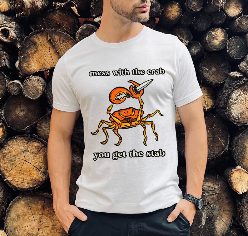 K&ouml;nnte beinhalten: Wei&szlig;es T-Shirt mit einem Grafikdruck eines Krabben, der ein Messer h&auml;lt. Der Text "mess with the crab you get the stab" ist auf dem T-Shirt aufgedruckt.