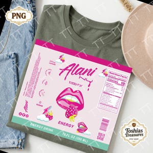 May include: An olive green t-shirt with a pink and white Alani Nu Berry Pop energy drink label. The label features a graphic of lips, a strawberry, and the text "Energy Drink" and "12 FL OZ (355 ml)".