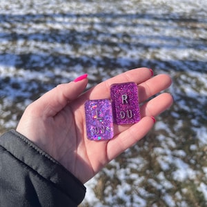 May include: A white ceramic mug with a black handle and the text "But First, Coffee" in a bold, black font. The mug is filled with a dark liquid, likely coffee, and sits on a light-colored surface.