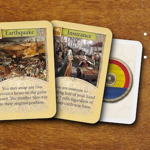 May include: Three rectangular game cards with cream-colored borders. The first card is titled Earthquake, the second Insurance, and the third features a circular shield with red, yellow, and blue stripes. Text on the cards explains game rules.