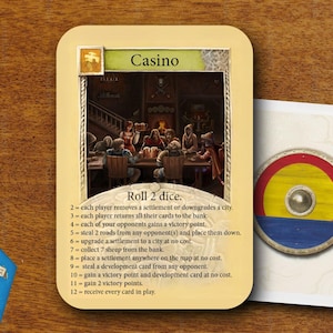 Pode incluir: Uma carta de jogo de tabuleiro intitulada Casino com uma ilustração de pessoas numa mesa e texto listando resultados para dois dados. Ao lado há uma carta com um escudo circular, um dado amarelo, um dado vermelho e peças de madeira azuis.