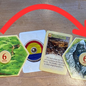 May include: Two hexagonal board game tiles with the number 6 and five dots, a circular token with red, yellow, and blue stripes, and a rectangular card labeled Earthquake with text describing a swap action, all under a red curved arrow.