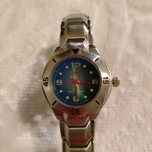 May include: A silver wristwatch with a blue face and silver hands. The watch has a silver metal band and a date window at the 3 o'clock position.