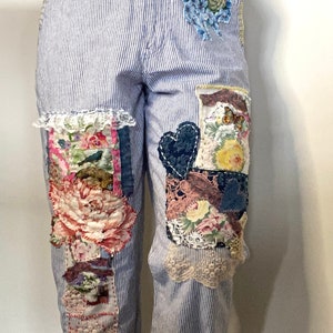 May include: Blue and white striped trousers with floral and lace appliques. The trousers have a cuffed hem and are made of a lightweight fabric.