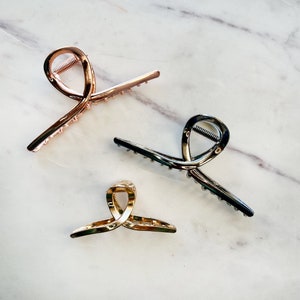 Puede incluir: Tres pinzas para el pelo en diferentes colores: dorado, dorado rosa y negro. Cada pinza tiene un diseño retorcido y una fila de dientes para sujetar el cabello.