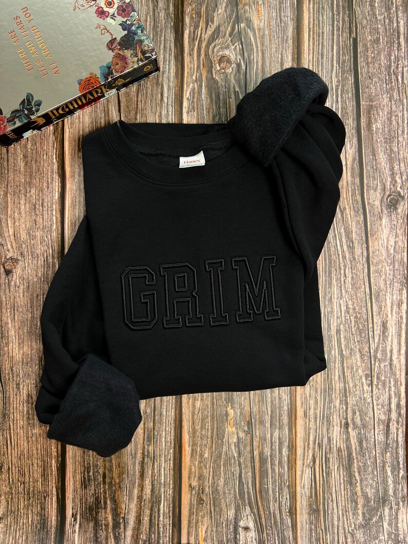 May include: Black sweatshirt with the word "GRIM" embroidered in black on the front.