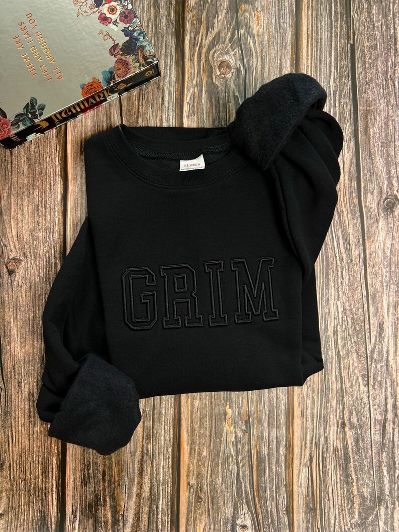 May include: Black sweatshirt with the word "GRIM" embroidered in black on the front.