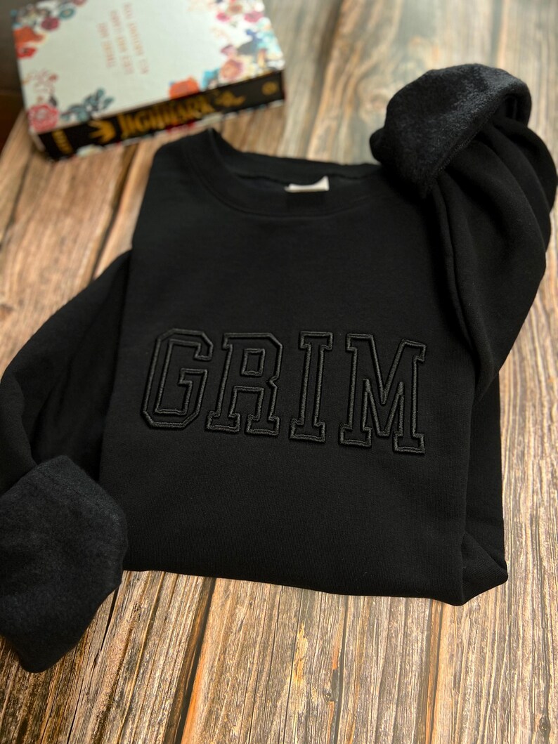 May include: Black sweatshirt with the word "GRIM" embroidered in black on the front.