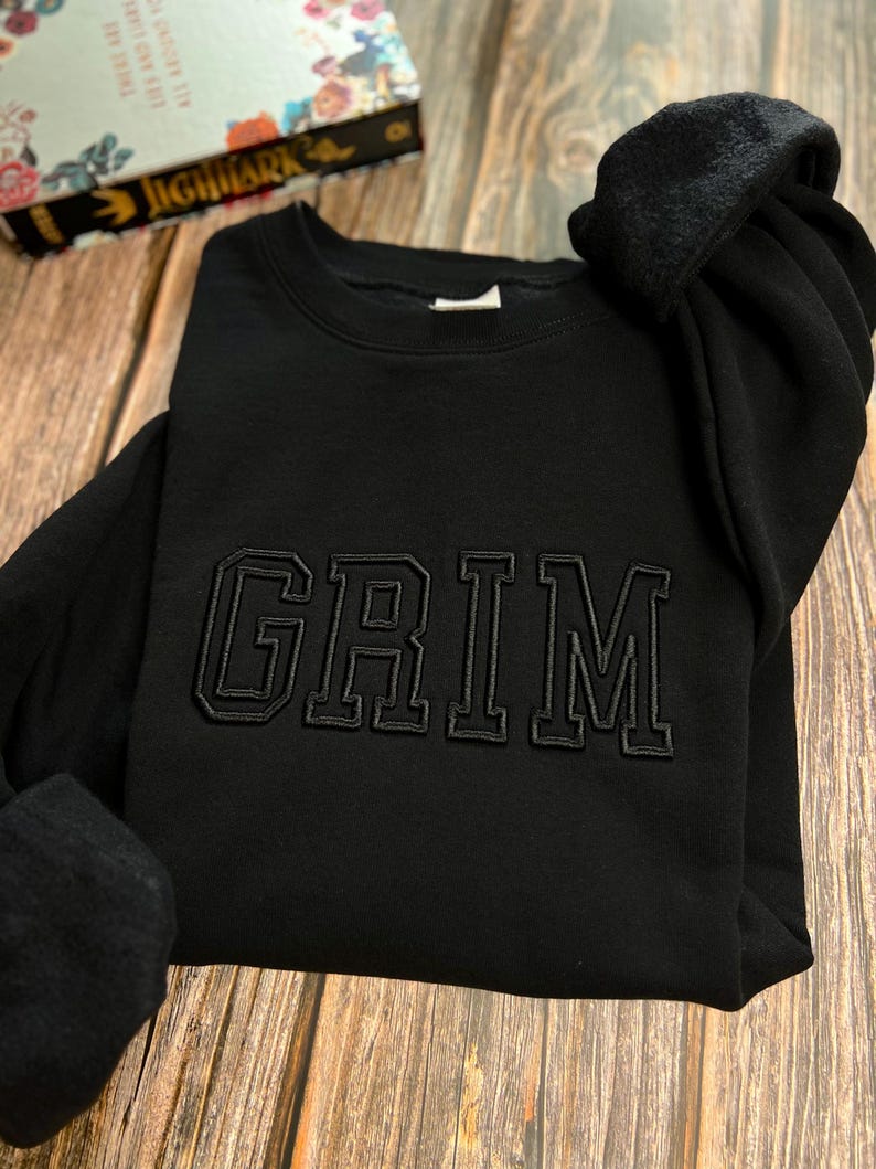 May include: Black sweatshirt with a black embroidered word "GRIM" on the front.