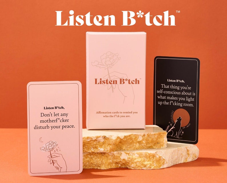 Puede incluir: Un juego de cartas de afirmaci&oacute;n rosa y negro con el texto "Listen B*tch" y varios mensajes empoderadores. Las cartas presentan ilustraciones de flores y un lobo.