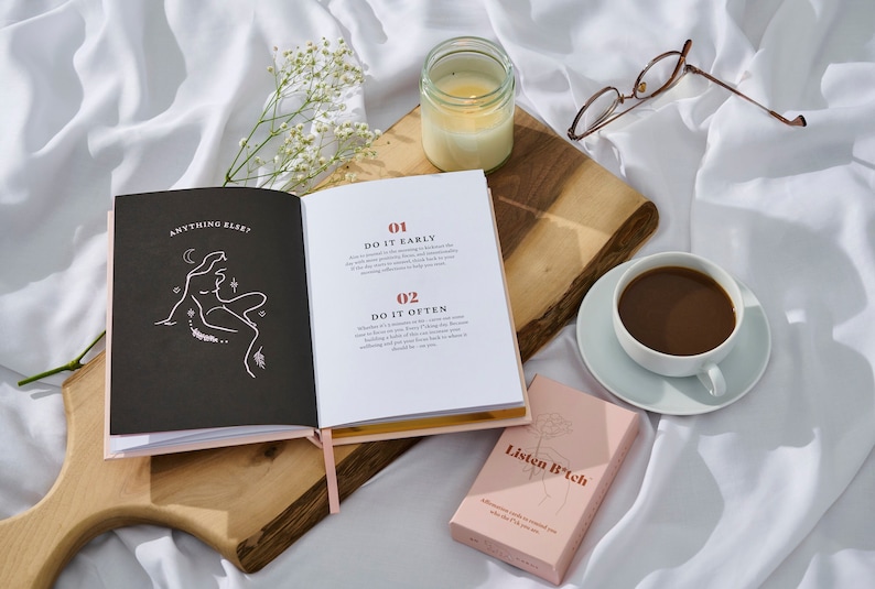 May include: Open book with the title "Anything Else?" and text that reads "01 Do It Early" and "02 Do It Often". A pink box with the text "Listen B*tch" is on a wooden surface with a white candle and a cup of coffee.