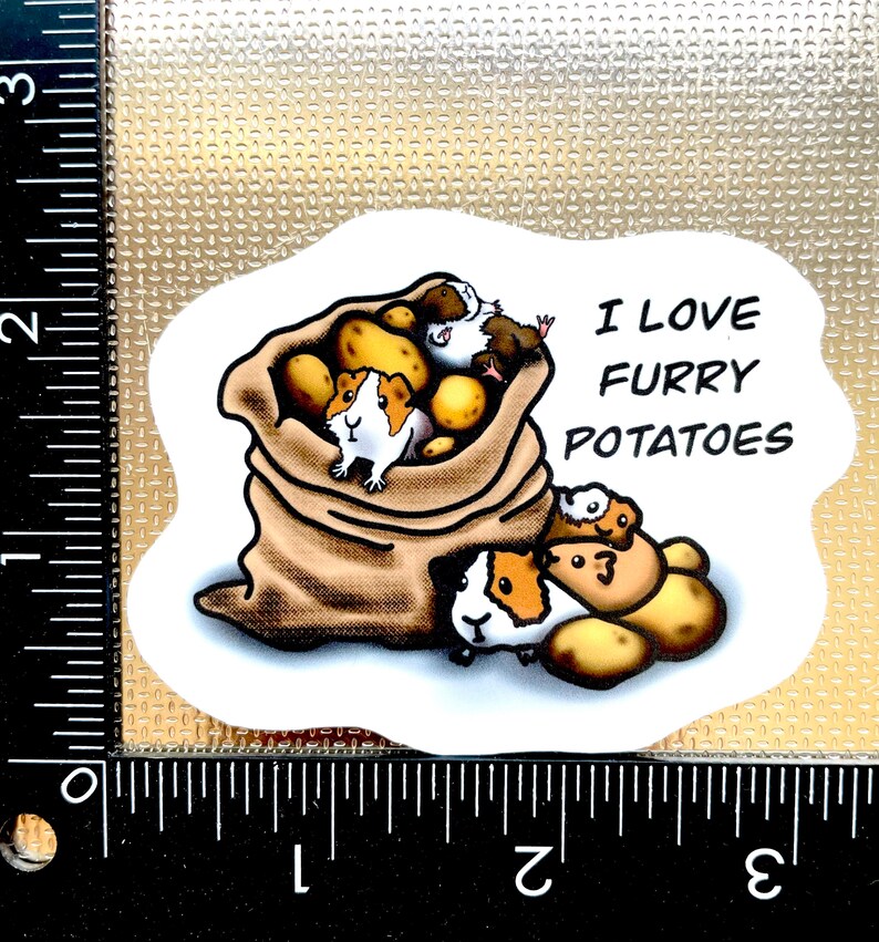 May include: A white sticker with a cartoon illustration of guinea pigs in a burlap sack with potatoes. The text "I love furry potatoes" is written in black.