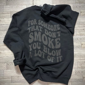 May include: Black sweatshirt with the text "For someone that don't smoke you blow a lot of it" in a retro font.