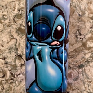 May include: A blue and white tumbler with a cartoon image of Stitch from Lilo & Stitch. The tumbler has a light blue base with a blue light.