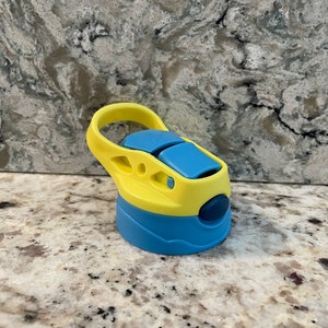 May include: A yellow and blue water bottle lid with a carrying handle. The lid has a blue button on the side.