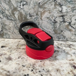 May include: A red and black water bottle lid with a carrying handle. The lid has a push button to open and close the spout.