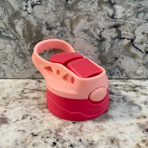 May include: Pink and red plastic water bottle lid with a carrying handle. The lid has a push button on the side.