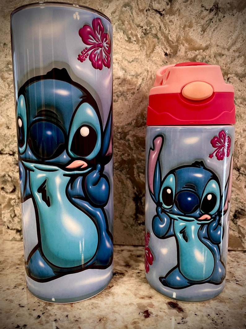 May include: Two stainless steel tumblers with a blue Stitch character from the Disney movie Lilo & Stitch. The tumblers have a light blue background with pink hibiscus flowers. The larger tumbler has a pink lid and the smaller tumbler has a pink lid with a pink straw.