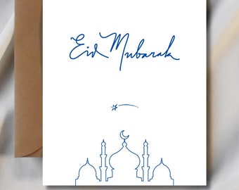Könnte beinhalten: Weiße Grußkarte mit blauem Schriftzug "Eid Mubarak" und einer Moscheen-Silhouette. Ein brauner Umschlag ist hinter der Karte zu sehen. Die Karte liegt auf einer weißen Satin-Oberfläche.