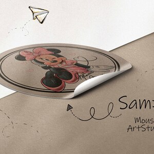 K&ouml;nnte beinhalten: Ein runder Aufkleber mit einem Cartoon-Bild von Minnie Mouse in einem rosa Kleid mit wei&szlig;en Punkten. Der Aufkleber l&ouml;st sich von einem braunen Papierhintergrund. Der Text "Sample Mouse Art Studio" steht unter dem Aufkleber.