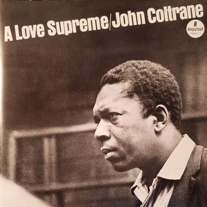 Może przedstawiać: Czarno-białe zdjęcie Johna Coltrane'a, znanego muzyka jazzowego, na okładce jego albumu "A Love Supreme". Okładka albumu zawiera tytuł albumu dużymi, pogrubionymi literami i nazwisko muzyka mniejszymi literami poniżej.