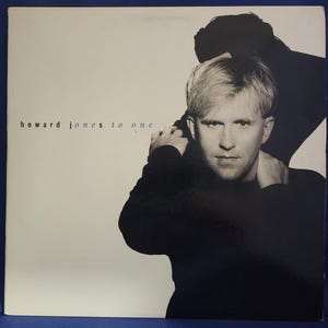 May include: Black and white album cover featuring a man with blond hair wearing a black shirt. The album title "howard jones to one" is printed in white on the cover.