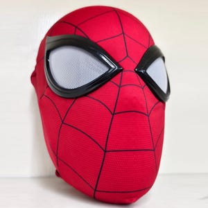 May include: A red Spider-Man mask with black webbing and large, white-mesh eye openings outlined in black. The mask is made of a textured fabric and is designed to cover the entire head.