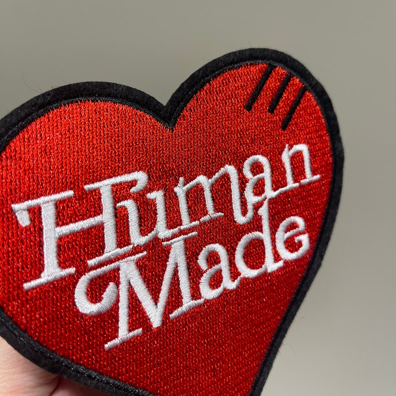 May include: Red heart-shaped embroidered patch with white text that reads "Human Made".